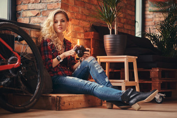 Sensual blonde hipster girl with long curly hair dressed in a fleece shirt and jeans holds a camera...