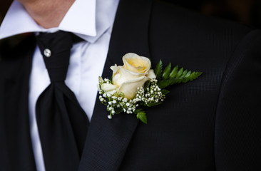 Dettaglio abito da sposo con camicia bianca, giacca nera, cravatta grigia, gilet e fiore nel bavero