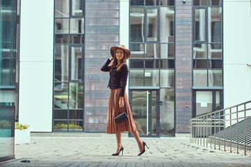Happy fashion elegant woman wearing a black jacket, brown hat and skirt with a handbag clutch...