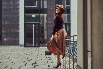 Smiling fashion elegant woman wearing a black jacket, brown hat and skirt with a handbag clutch...