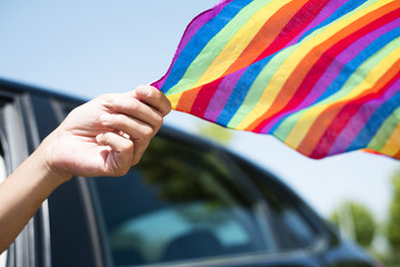 man in a car waving a rainbow flag.