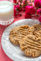 Plate of peanut butter cookies with milk and flowers in the background