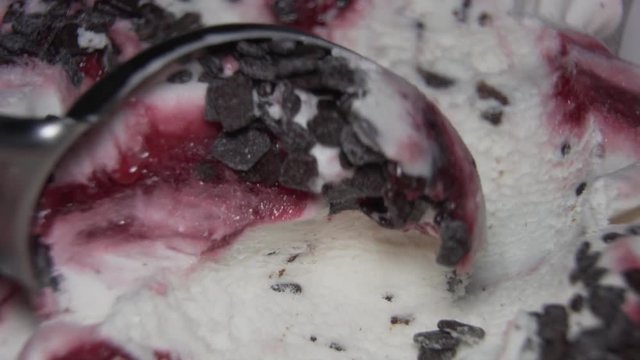 Ice-cream with cherry jam and chocolate pieces being scooped with a spoon. Close up