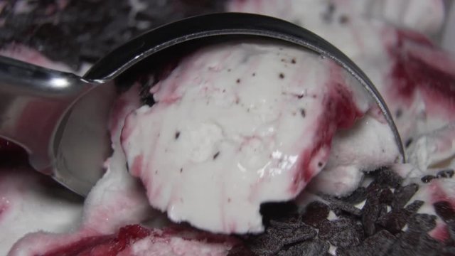 Ice-cream with cherry jam and chocolate pieces being scooped with a spoon. Close up