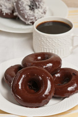 Top view, medium distance of homemade, freshly baked, four chocolate donuts with chocolate frosting on a white, round plate and a cup of espresso 