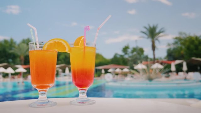 Two cool cocktails stand on the table on the background of the pool and palm trees. Paradise and luxury resort