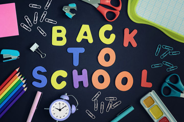 In the center of a black background with colored letters lined inscription Back to School. Around are stationery and school supplies.