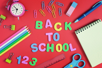 On a red background, color pencils, paper clips and scissors are arranged in a circle. In the center the inscription is BACK TO SCHOOL made in colored letters. School supplies .