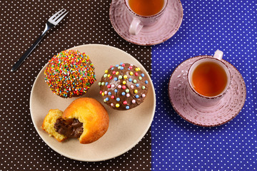 Baking with tea and chocolate on the table.  Two cups of tea with cupcakes and chocolate with a multicolored powder on the table.