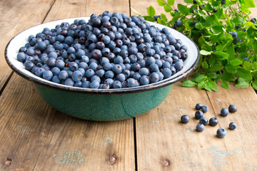 Fototapeta na wymiar Fresh Bilberries from a bowl on old wooden table. Leaves with berries Bilberries on the Bush