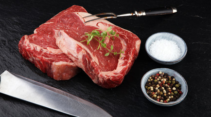 Raw fresh meat Ribeye Steak, seasoning and meat fork on dark background