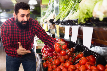 Glad male seller offering tomatoes in shop