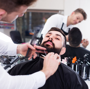 Ordinary guy creating shape for beard of client