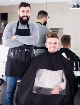 positive guy stylist demonstrating final haircut to client at hairdressing salon