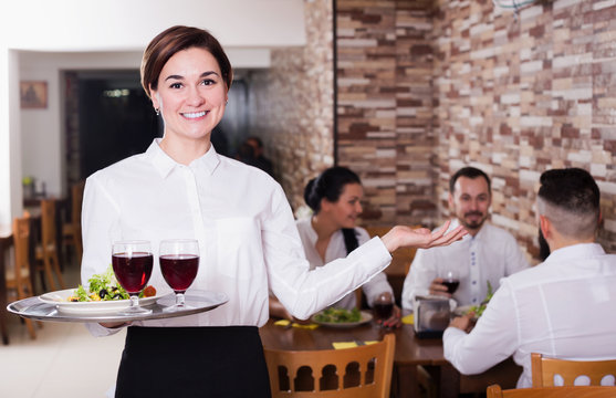 Smiling woman waiter carrying order for visitors