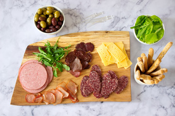 Appetizer table for wine or beer with sausages, dried meat and cheese, served with grissini, herbs and olives.