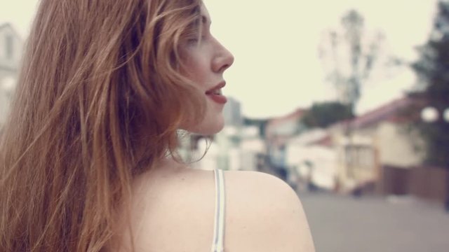 Follow me. Girl running forward from the back. Girl turns around and playfully looks into the camera, straightens her hair. She's smiling. Lovely lilo with freckles. Woman is walking along the street.