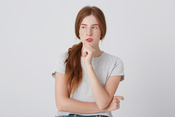 Portrait of thoughtful beautiful redhead young woman with freckles thinking and looking to the side isolated over white wall