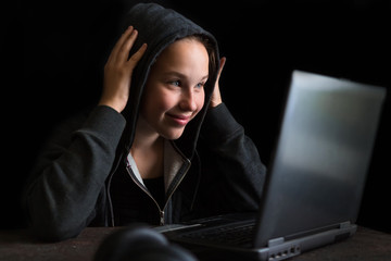 Girl teenager in a hood playing a computer game on a dark background with copy space selective focus, concept of technology and video games