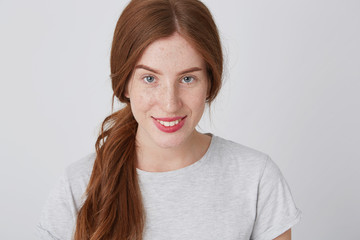 Closeup of cheerful pretty redhead young woman with freckles looking at camera and smiling isolated over white background
