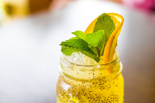 Fresh tropical yellow non-alcoholic cocktail with chia seeds in a mason jar decorated with slice of orange and peppermint - drinks, people and lifestyle concept