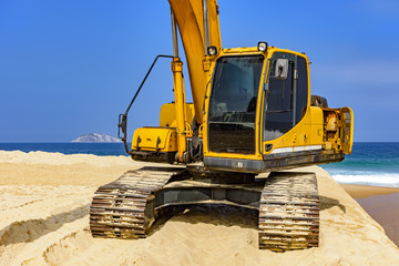 Obraz premium Yellow excavator cabin and arm over sand at beach in a sunny day