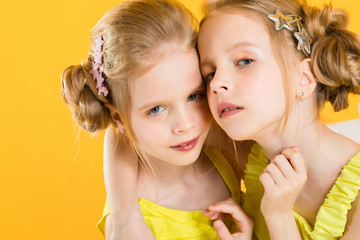 Twins girls are sitting on a chair on a yellow background.