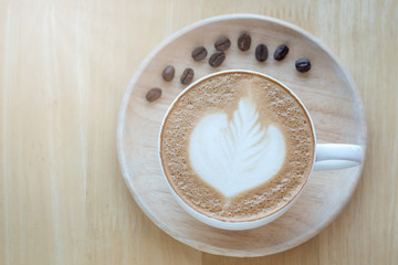 Latte art coffee and coffee beans in the morning time with sunlight on table wooden background.