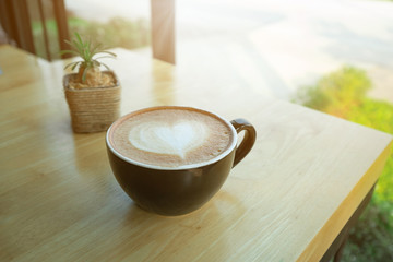 Latte art coffee in the morning time with sunlight on table wooden background.