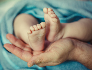 Baby feet in father hands. Ded or grendfather, grendmather and Child. Feet under the protection of the palms. Happy Family concept, conceptual image of maternity