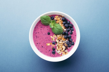 Smoothie bowl with granola, blueberries and mint on blue background. Healthy breakfast, top view.