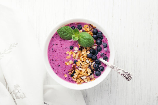 Smoothie bowl with granola, blueberries and mint on wooden table with napkin. Healthy breakfast, top view.