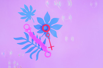 Obraz na płótnie Canvas Bubble wands on a pastel purple background with tropical leaves and copy space. Summer flat lay header in pink.