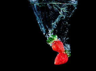 Red strawberry dropped into the water with splash on a black background