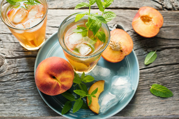Refreshing iced tea with ripe peaches on rustic background, selective focus, toned image
