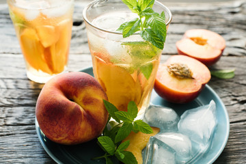Refreshing iced tea with ripe peaches on rustic background, selective focus, toned image