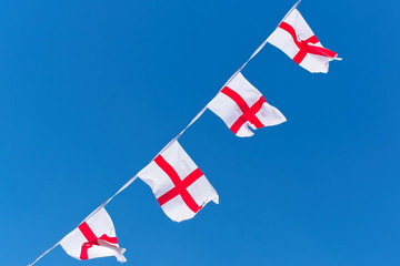 Single row of England flags / bunting flying against blue sky.