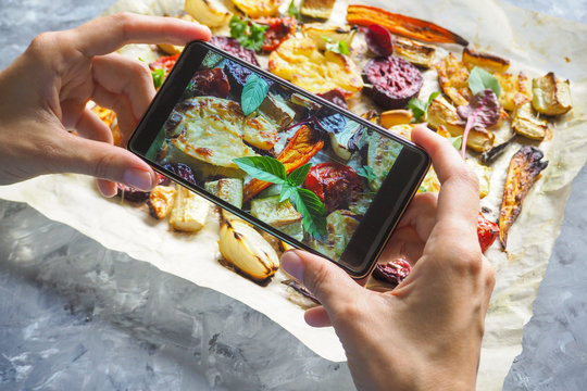 Female hands taking photo of food with mobile phone. Baked vegetables on parchment.