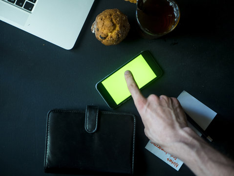 Top View Of Finger Scrolling Mobile Smartphone On Dark Table With Laptop And Note