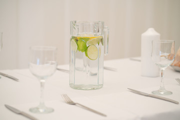 a delicious fresh drink of water with lime and mint stands on a table with a white tablecloth and empty dishes