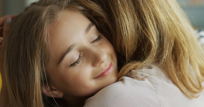 Close up of the pretty blonde teen girl hugging her mother and smiling. Portrait. Indoors.