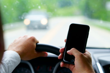 Don't text and drive ! A man is texting with a finger while a car is arriving in front.  focus on...