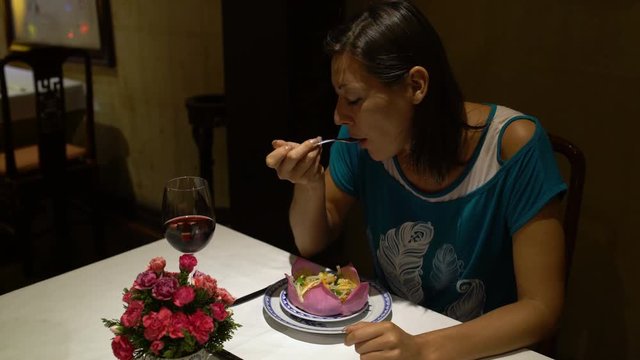 Girl sitting at the table eating the dish in the form of a Lotus Flower and drinking red wine