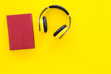 Distance education, e-learning concept. Headphones near hardback book with empty cover on yellow background top view copy space