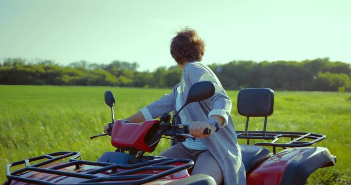 Adult woman driving a quad bike in a field drives out on a country road