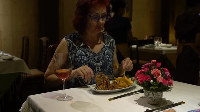 Woman sitting at the table eating the dish in the form of a Lotus Flower and drinking red wine