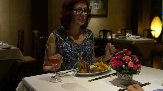 Woman sitting at a table in the restaurant eating, talking, chokaetsja a glass and drinking red wine