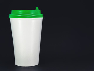 white plastic coffee cup with green lid on black background, front view with copy space