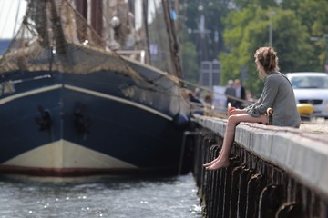 junge Frau sitzt alleine am Hafen
