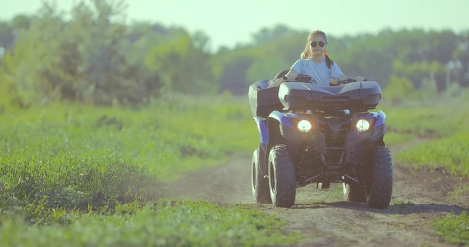 Little girl sits behind the wheel of ATV and rides off-road